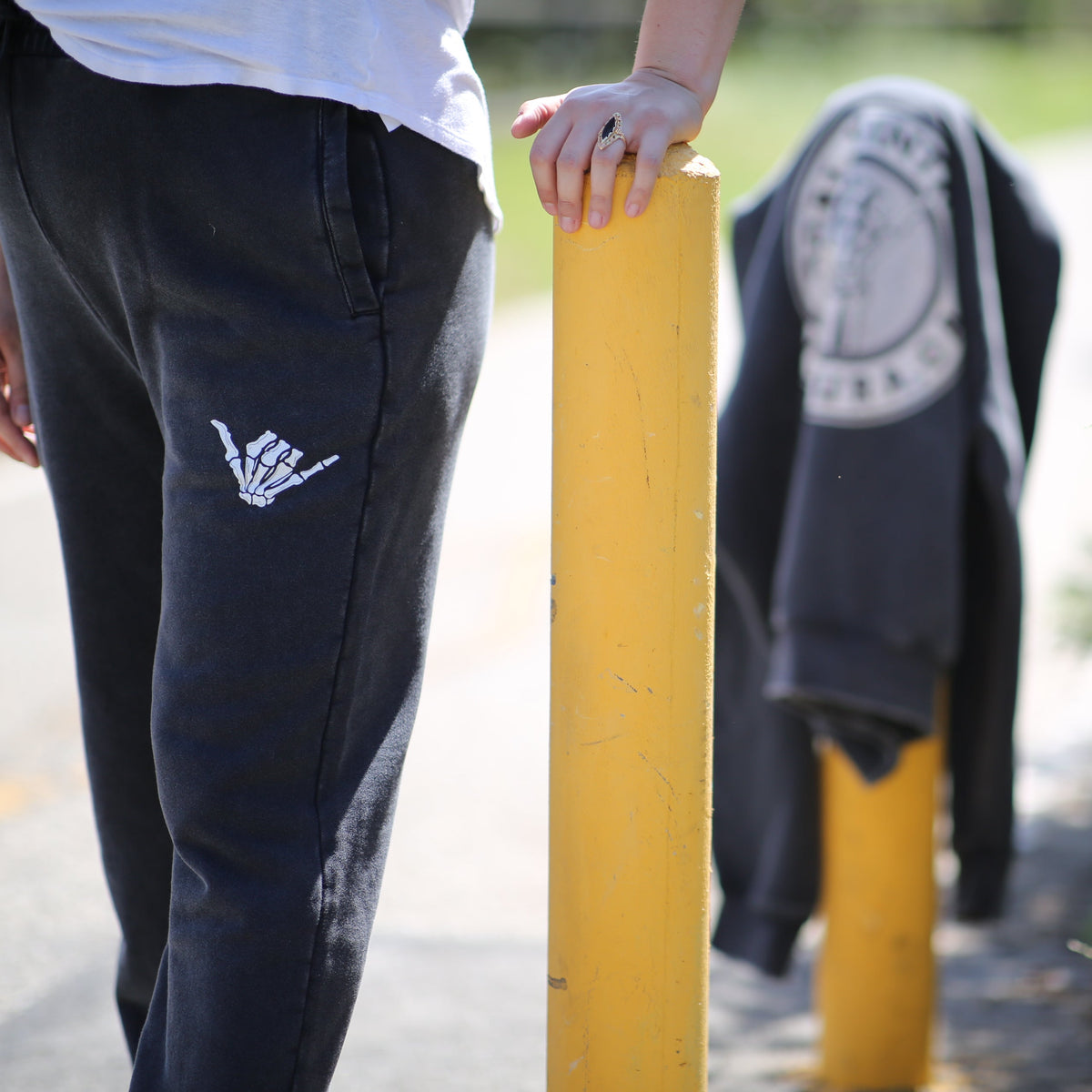 Person wearing black pants with a white logo, standing next to a yellow pole and fire hydrant.